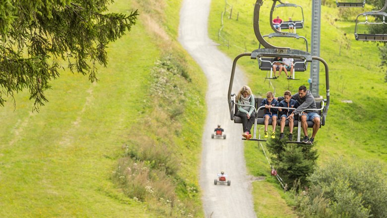 Family on chair lift over green landscape.