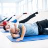 A group of people doing side leg raise exercises on mats in a bright room.