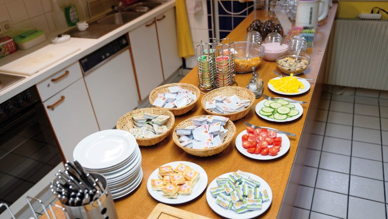 Breakfast buffet with plates, cutlery, spreads, vegetables and muesli.