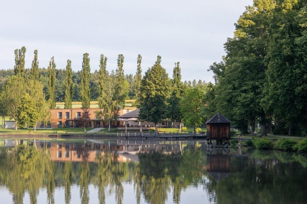 Lake with shore building and trees, peaceful landscape scene.