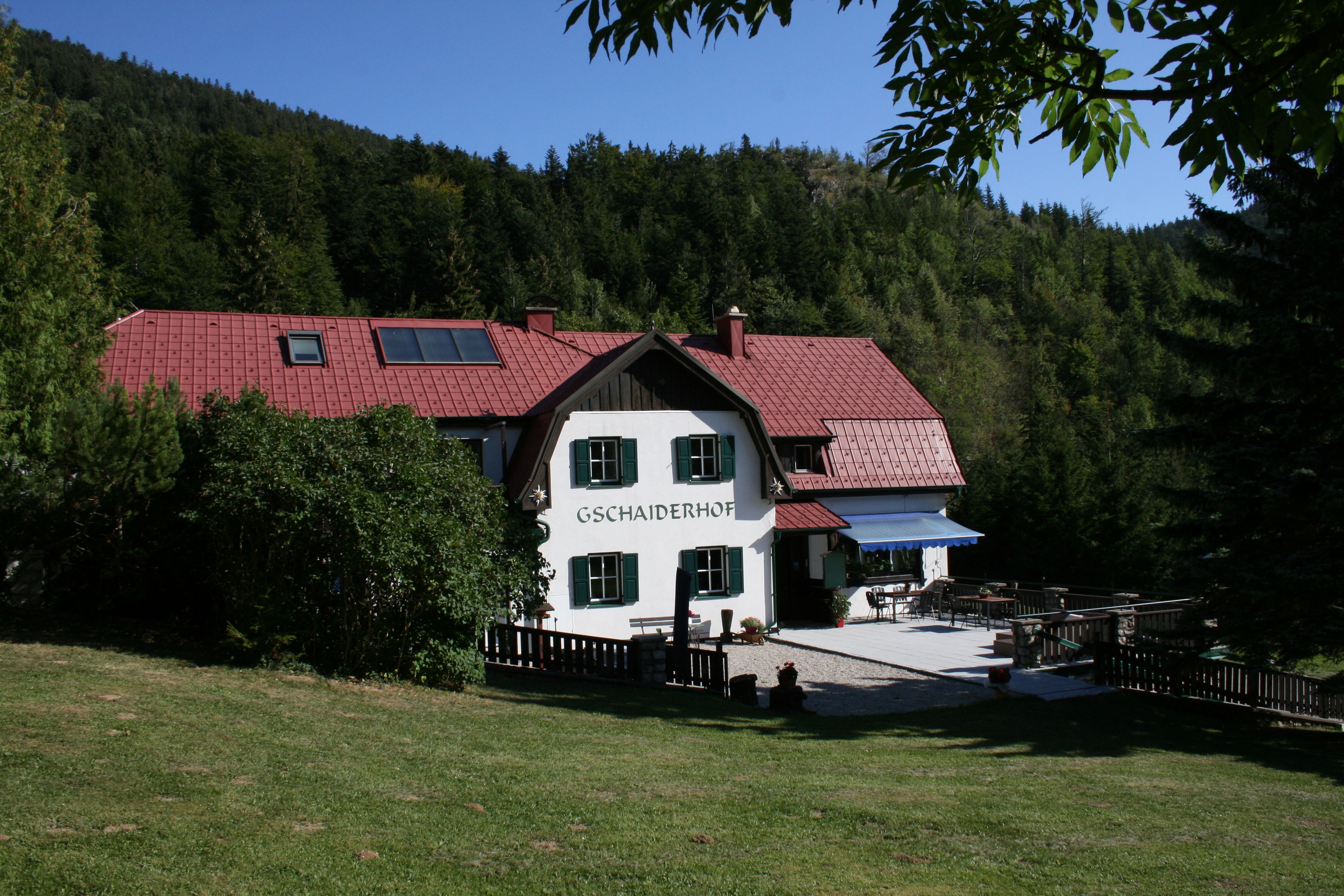 A traditional house with a red roof, surrounded by forest and meadow, with the inscription 'Gschaiderhof'.