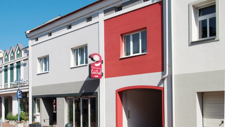Pension Central, © dh Facade of the Pension Central with gray and red walls, a sign and windows.