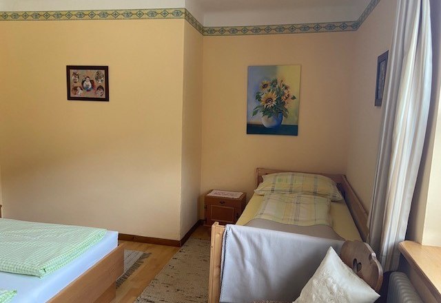 A room with two beds, a single bed and a double bed, decorated with pictures of flowers on the walls.