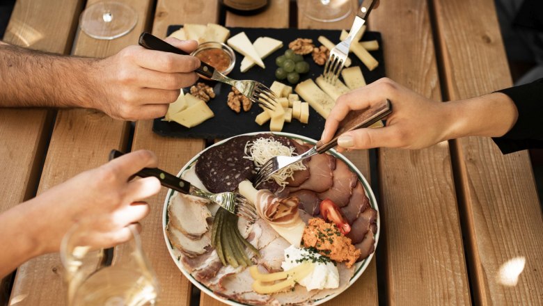 A table with a bottle of wine, glasses, cheese platter and cold cuts.