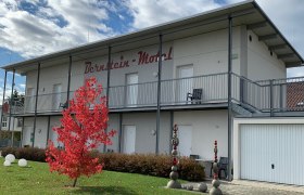 Two-story building with the inscription 'Bernstein Motel', red tree in the foreground, blue sky with clouds.