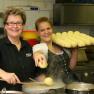 Two women in a kitchen, one holding a tray of dumplings, the other cooking dumplings in a pot.