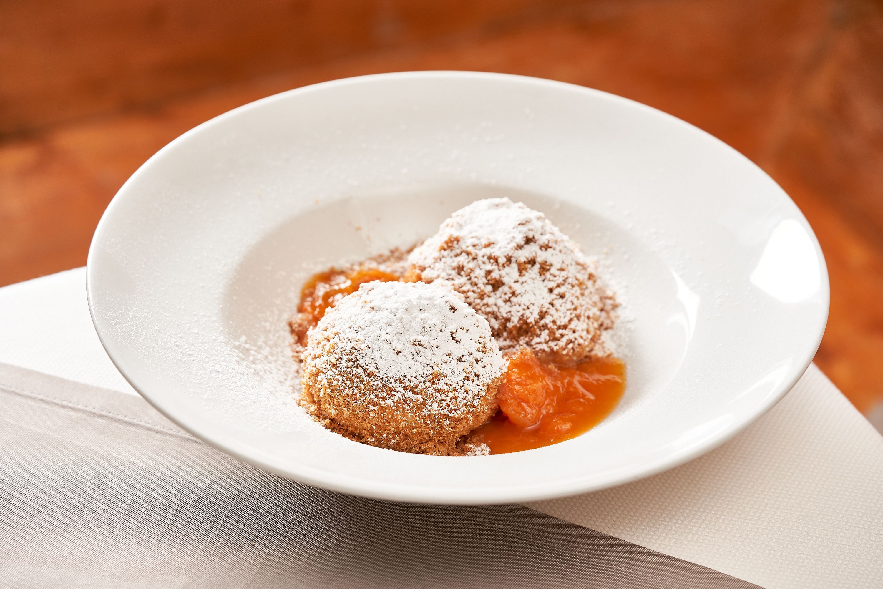 Two apricot dumplings with powdered sugar on a white plate.