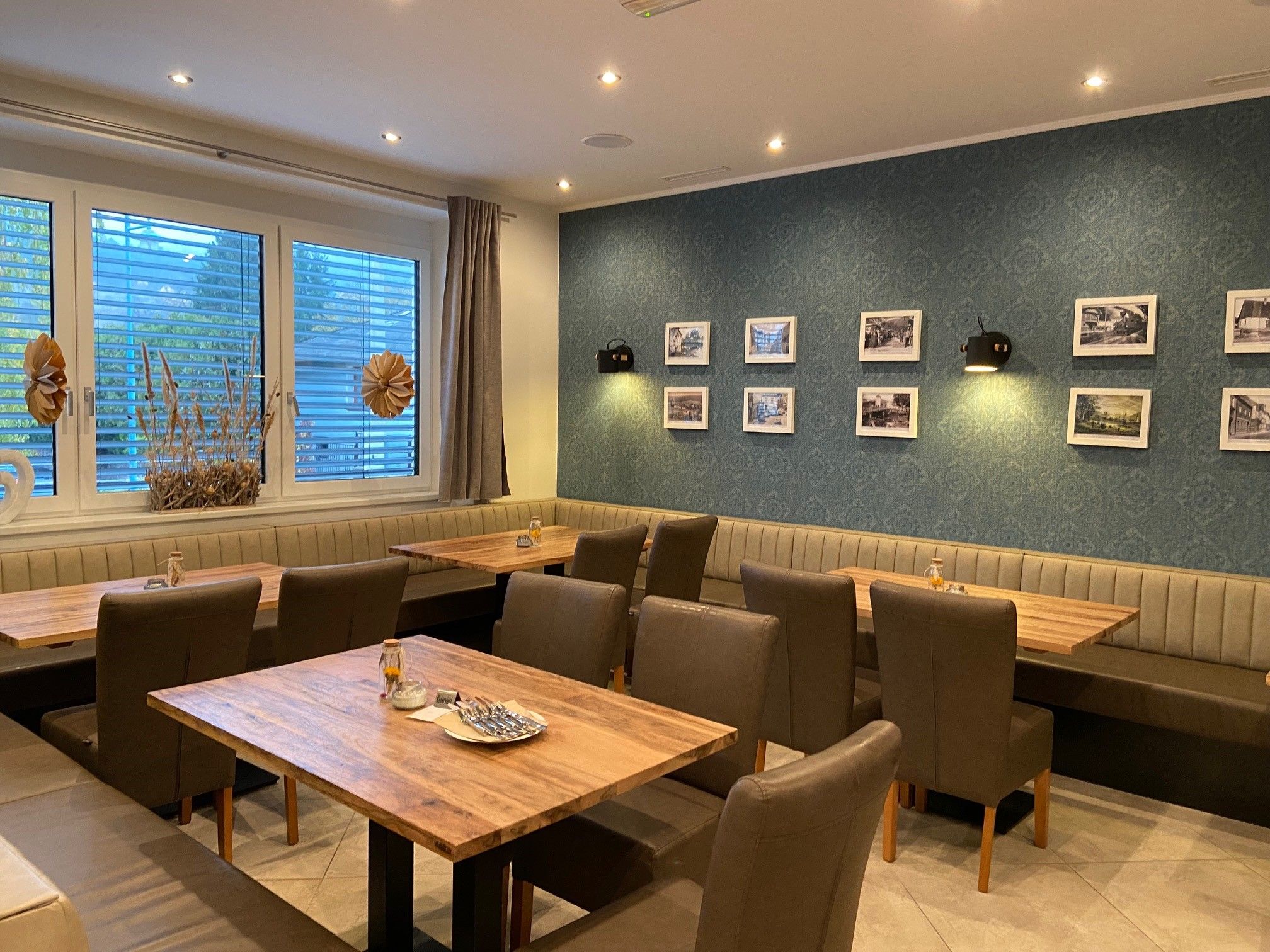 Interior view of a restaurant with wooden tables, upholstered chairs and a wall with framed pictures.
