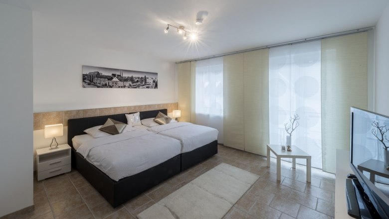 Modern bedroom with two beds, bedside tables, a picture on the wall and a TV.