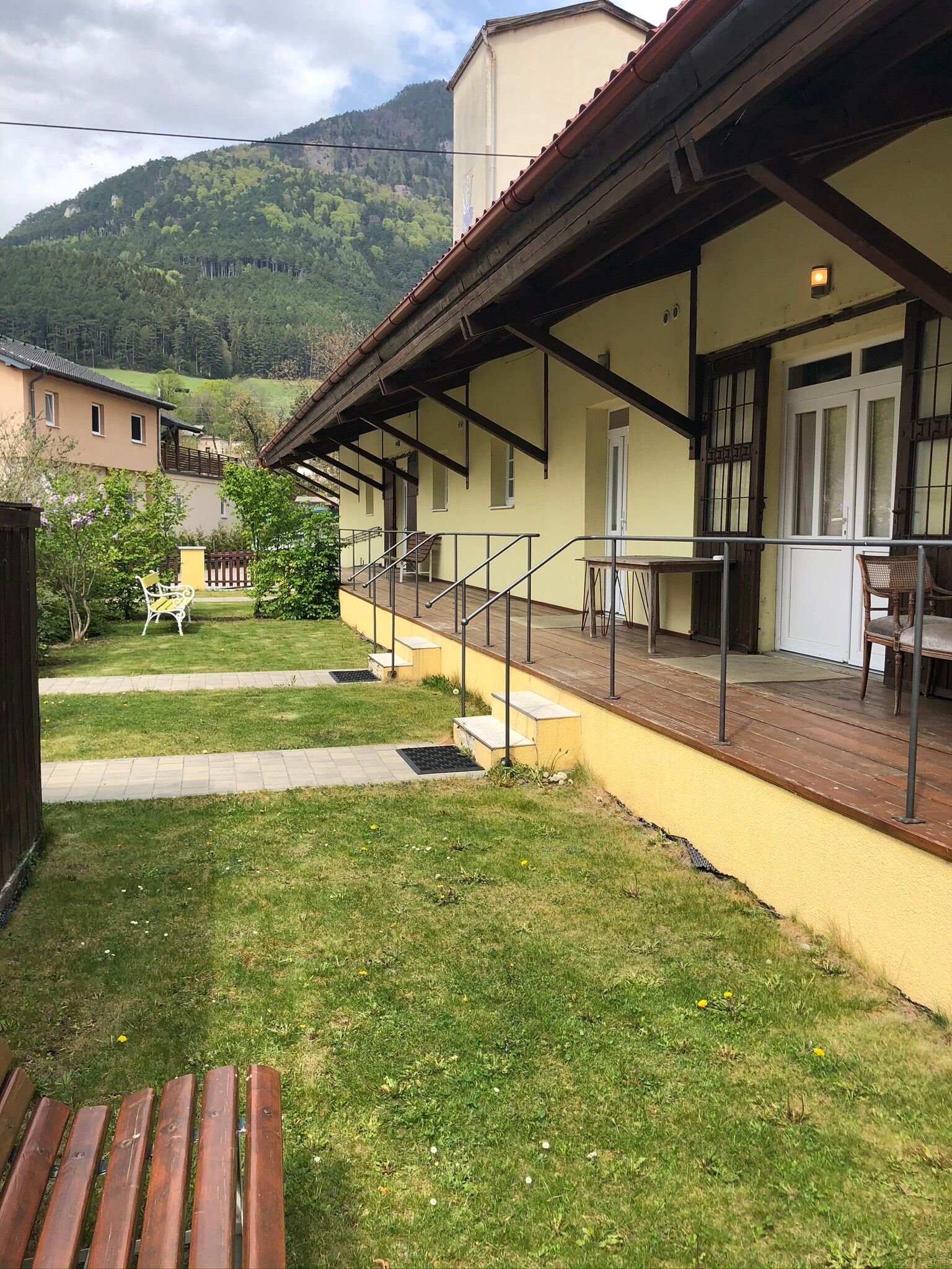 Exterior view of a yellow building with veranda and mountain in the background.