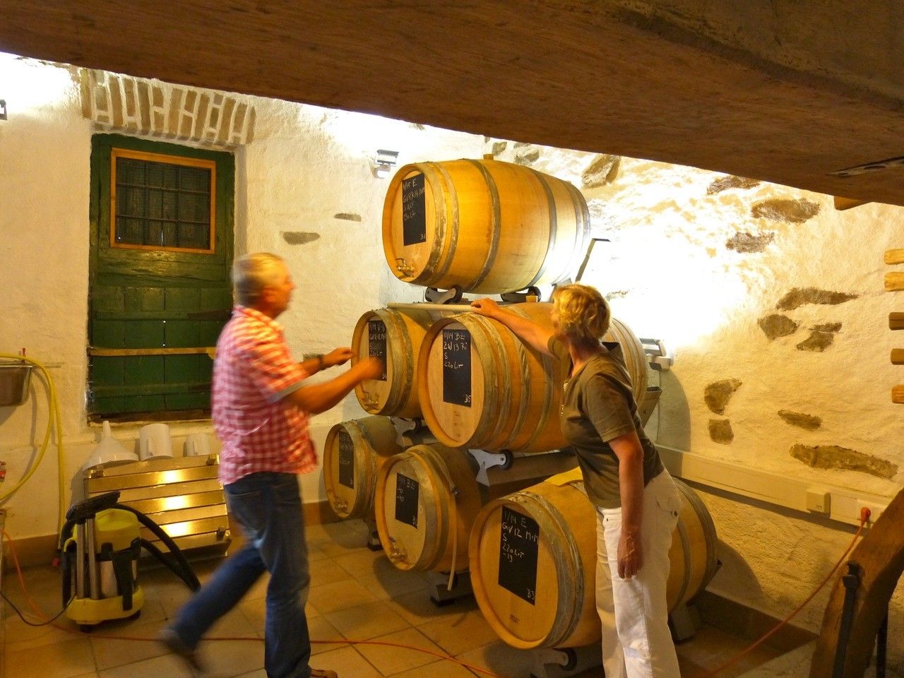 Two people in a wine cellar with wooden barrels.