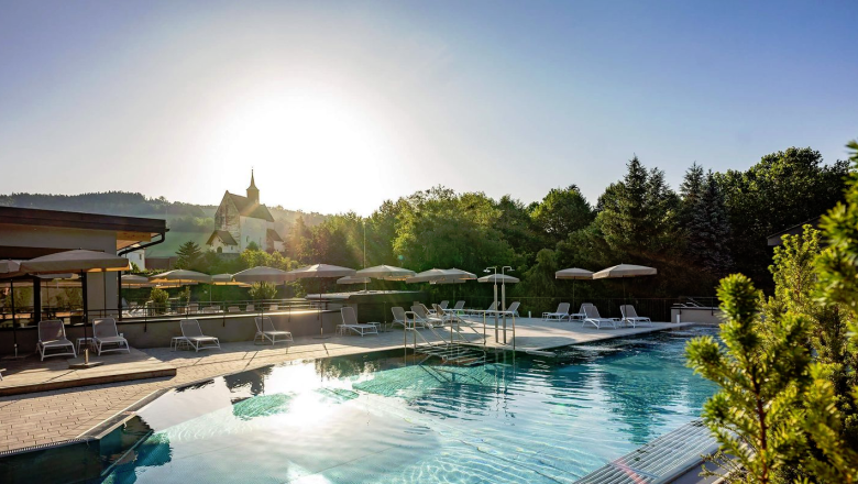 Outdoor area of a hotel with pool, sun loungers and umbrellas, surrounded by trees.