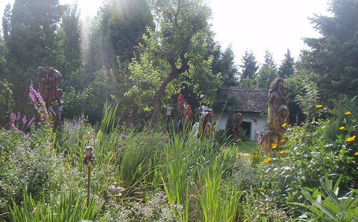 A lush garden with sculptures, trees and a small building in the background.
