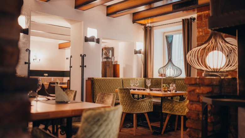 Cozy restaurant with wooden beams, green upholstered chairs and decorative lamps.