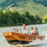 Group of people on a wooden boat on the Danube with a green landscape in the background.