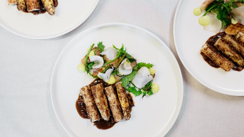 Three plates with artfully arranged gourmet dishes on a white tablecloth.