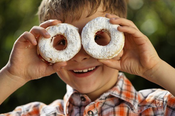 A boy holds two doughnuts sprinkled with powdered sugar in front of his eyes.
