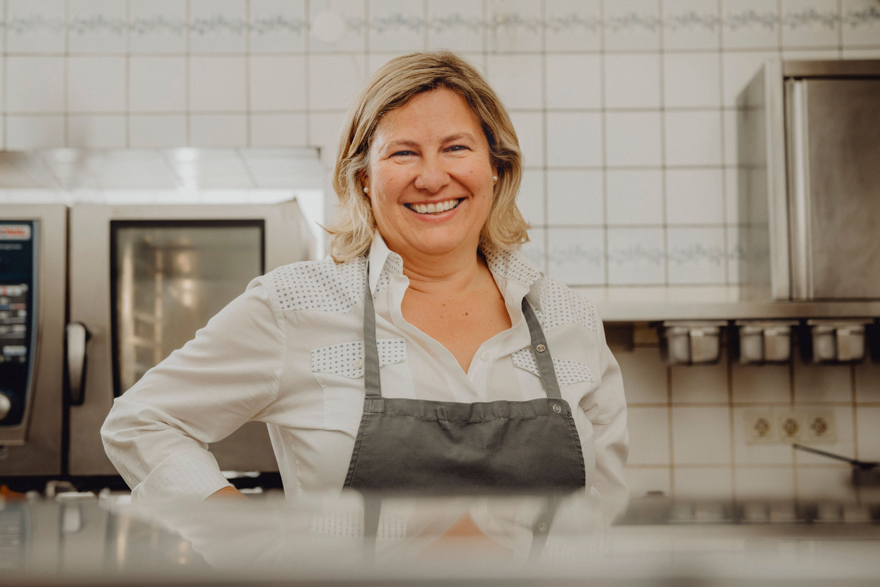 A smiling woman in a kitchen wearing an apron.