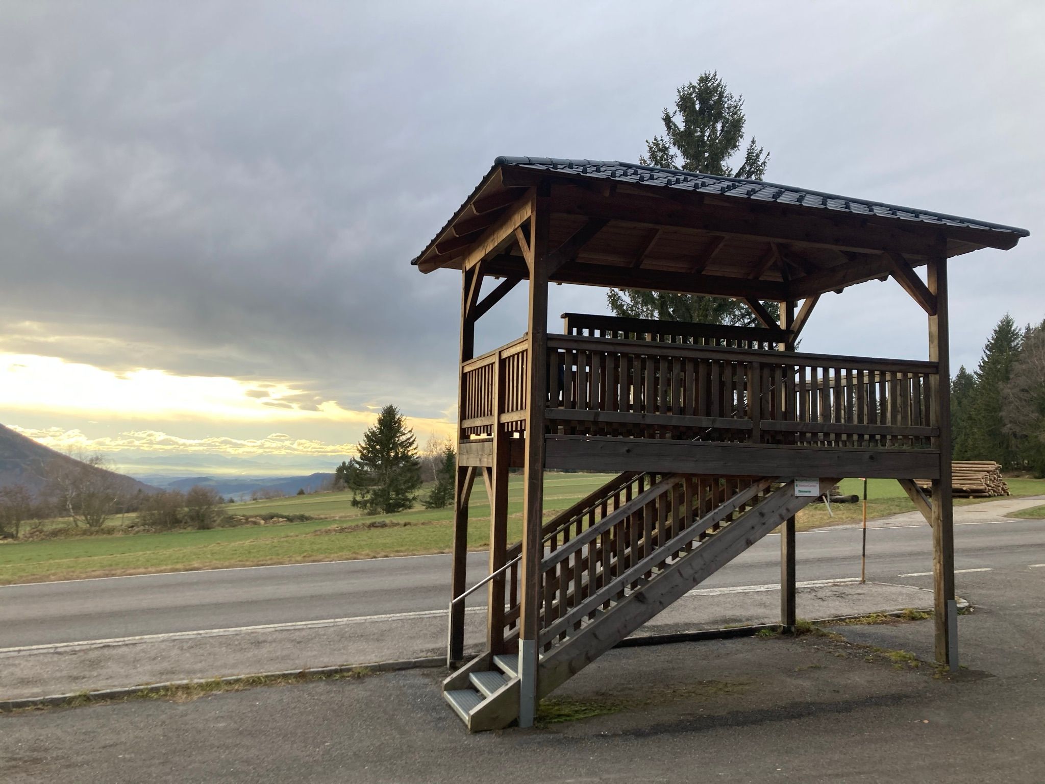 Wooden viewing platform with a view of a landscape and cloudy sky.
