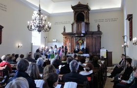 Interior view of a church during a service with a choir and a preacher at the altar.