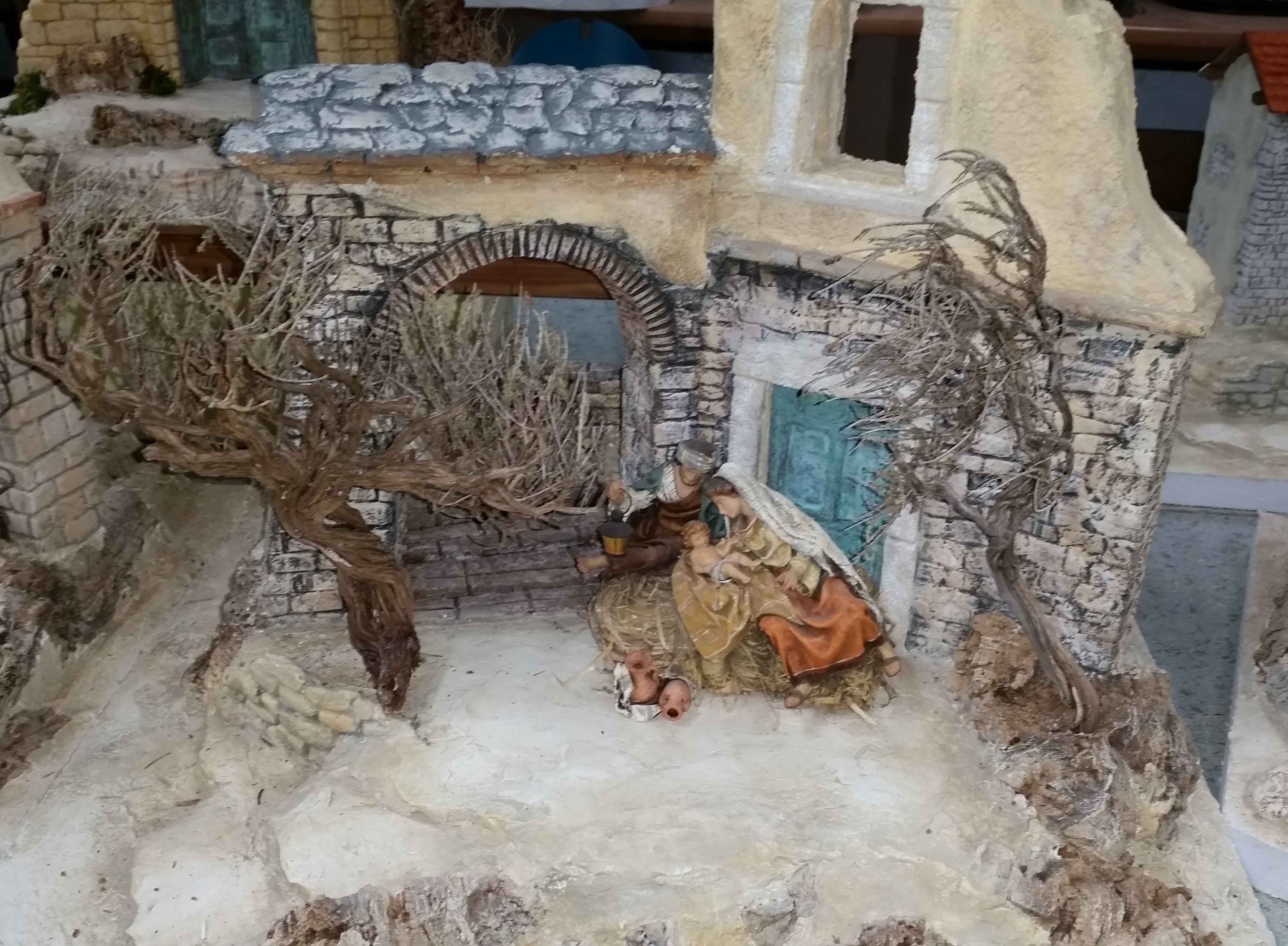 Oriental nativity scene with figures under an archway, surrounded by trees and buildings.