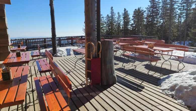 Wooden terrace with benches and tables, surrounded by snow and trees.