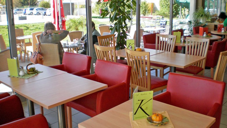 Interior view of a café with red armchairs and wooden tables, view of terrace with parasols.