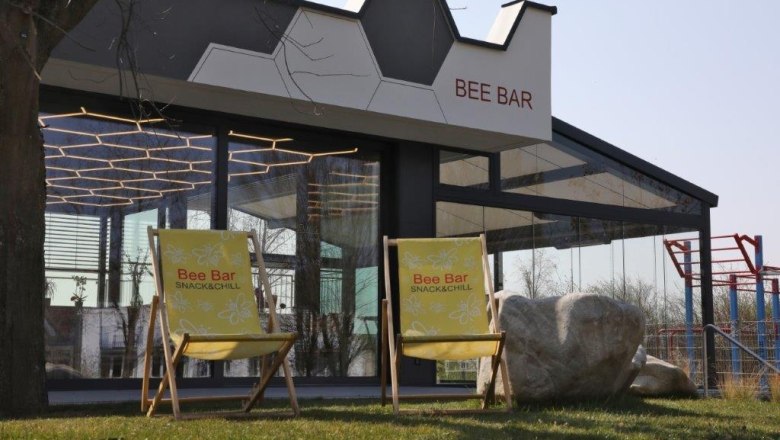 Two yellow deckchairs in front of the Bee Bar with its glass fa&ccedil;ade and geometric roof.