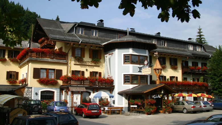 A traditional inn with flower-decorated balconies and parked cars in front of it.