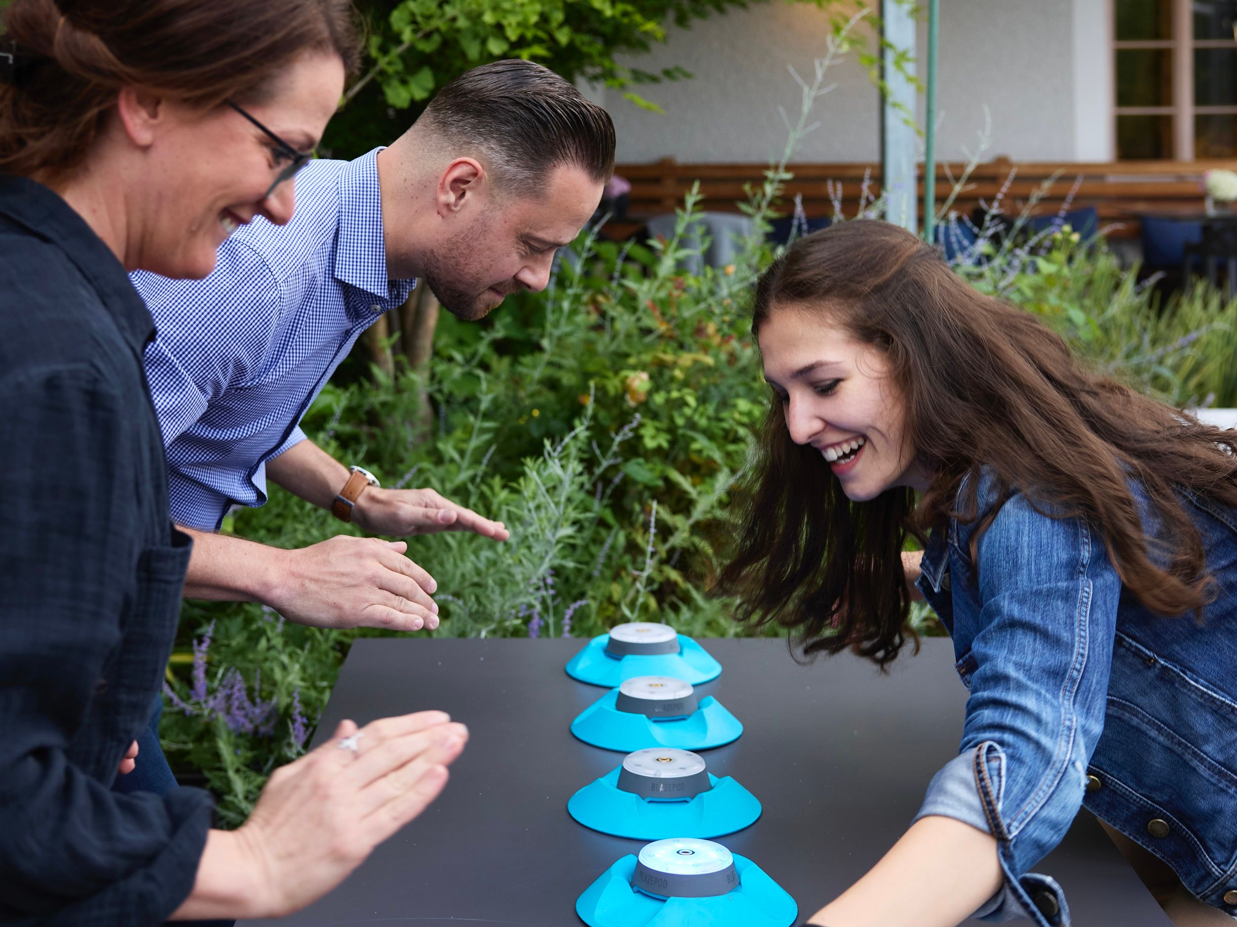 Three people play an outdoor reaction game with blue buttons.