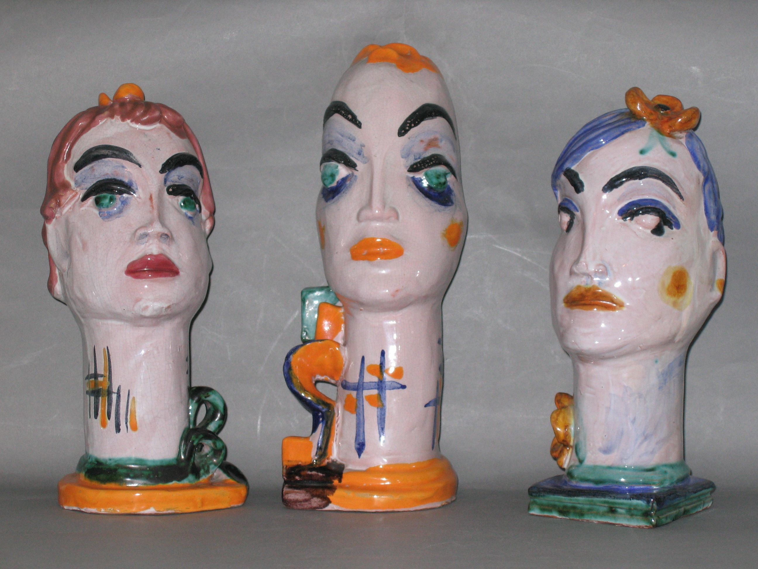 Three colorful ceramic busts with abstract faces on a grey background.