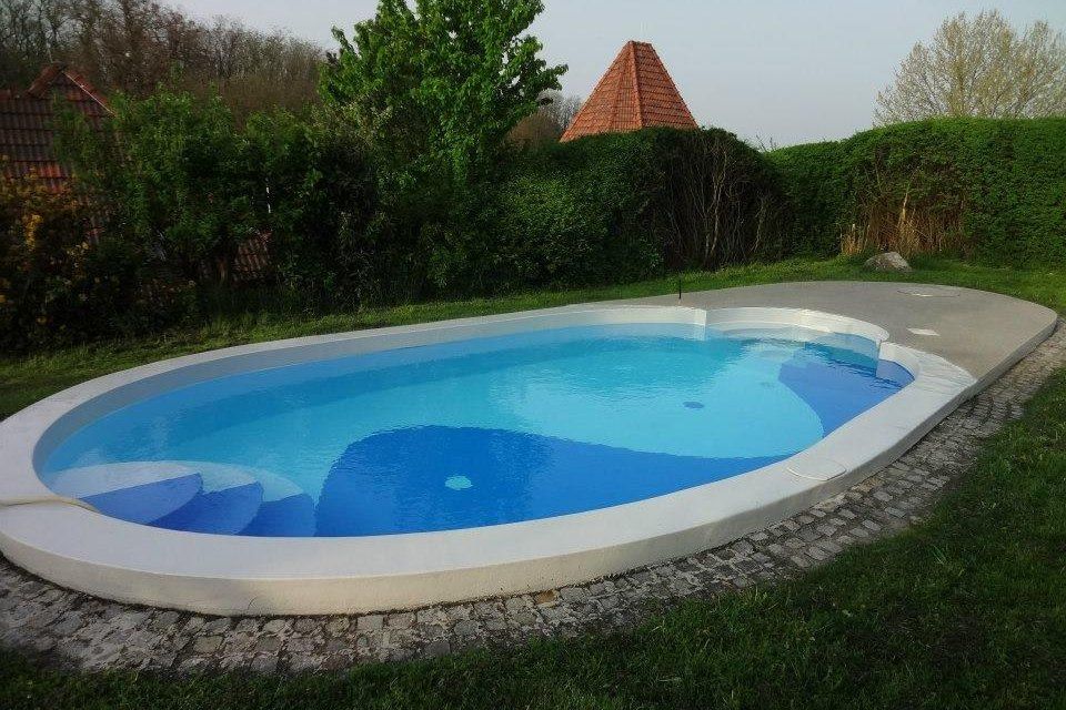 An oval pool in the garden with a blue water surface, surrounded by lawn and shrubs.