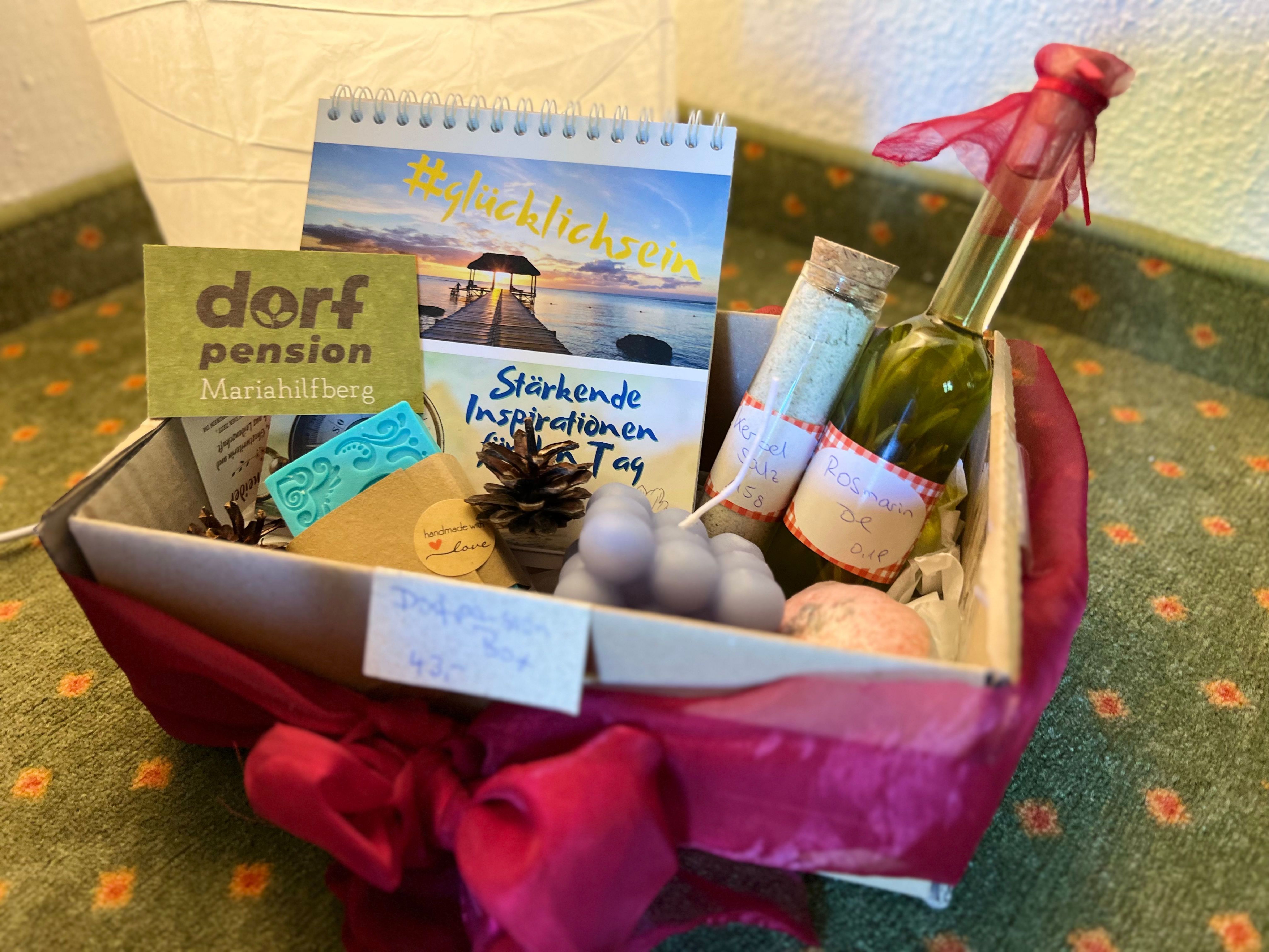 A gift basket with various wellness products, including a calendar, a bottle of oil and handmade soaps.