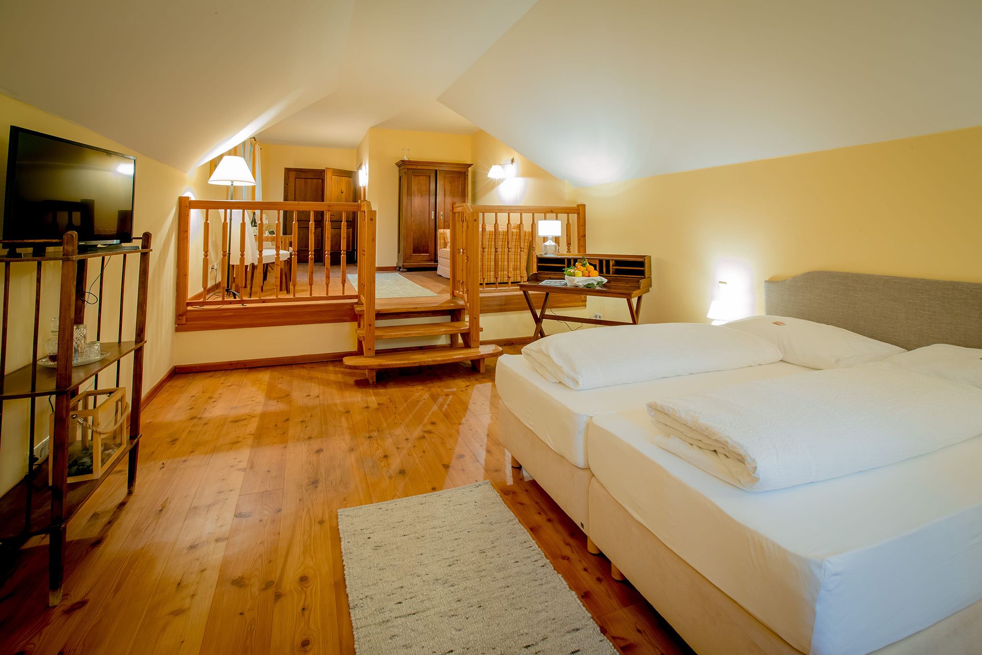 A cozy hotel room with a double bed, wooden floor and a small table with fruit.