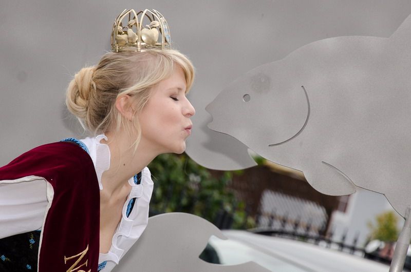 Woman with crown kisses carp sculpture.