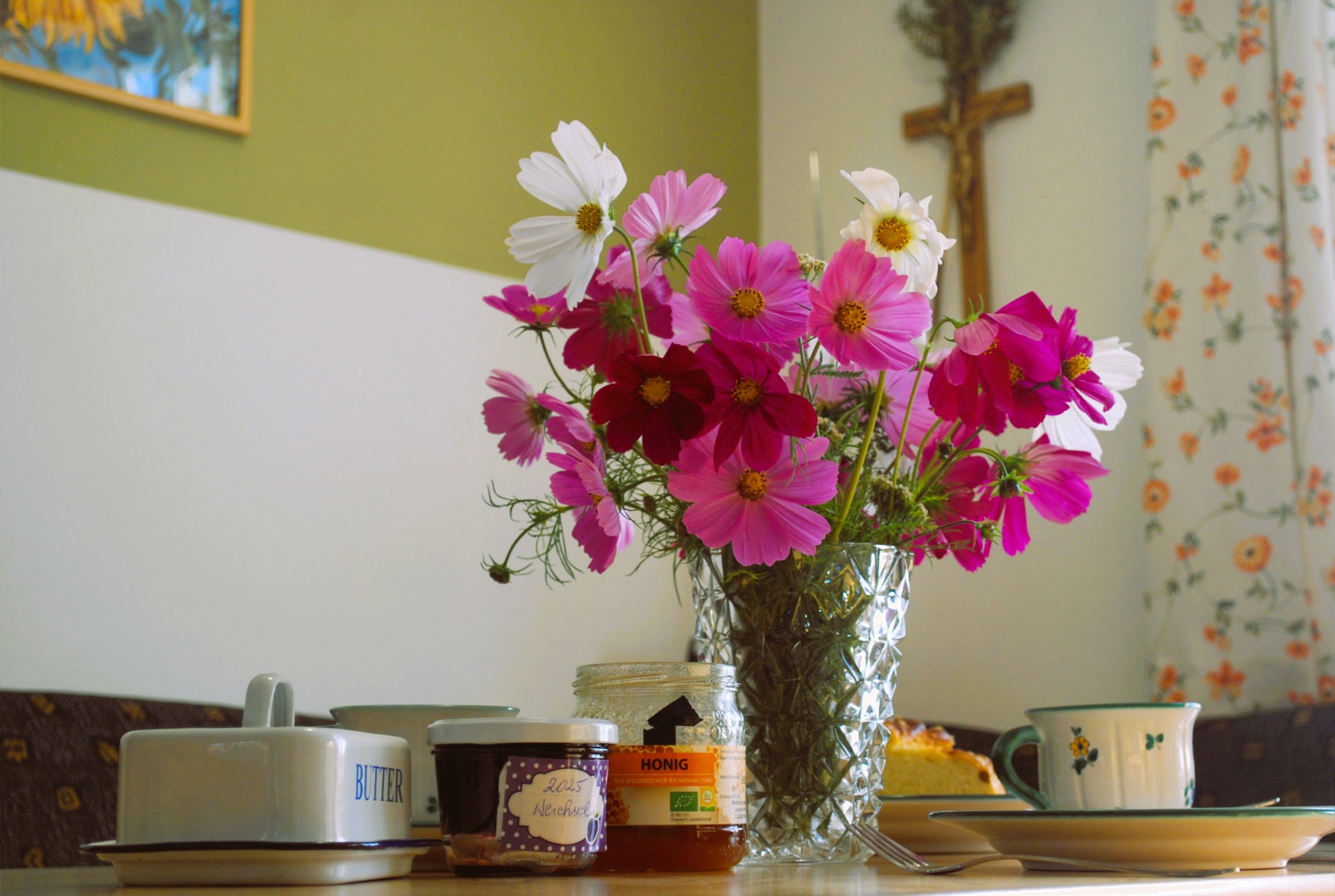 A breakfast table with a bouquet of flowers, jam, honey and crockery.
