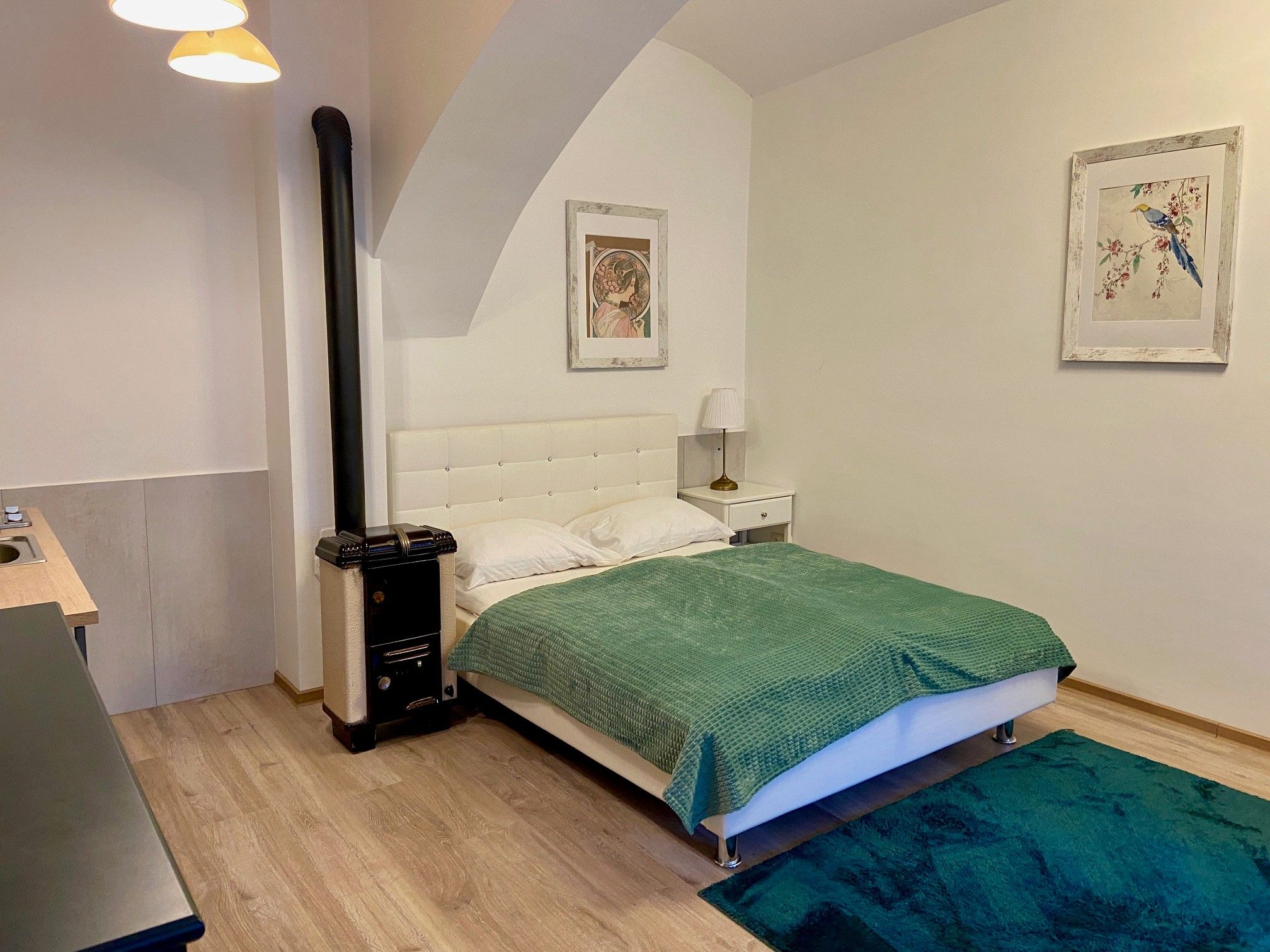 A cozy bedroom with a white bed, green ceiling, carpet and two pictures on the wall.