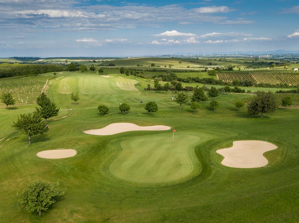 Aerial view of a golf course with green areas, sand bunkers and surrounding fields.