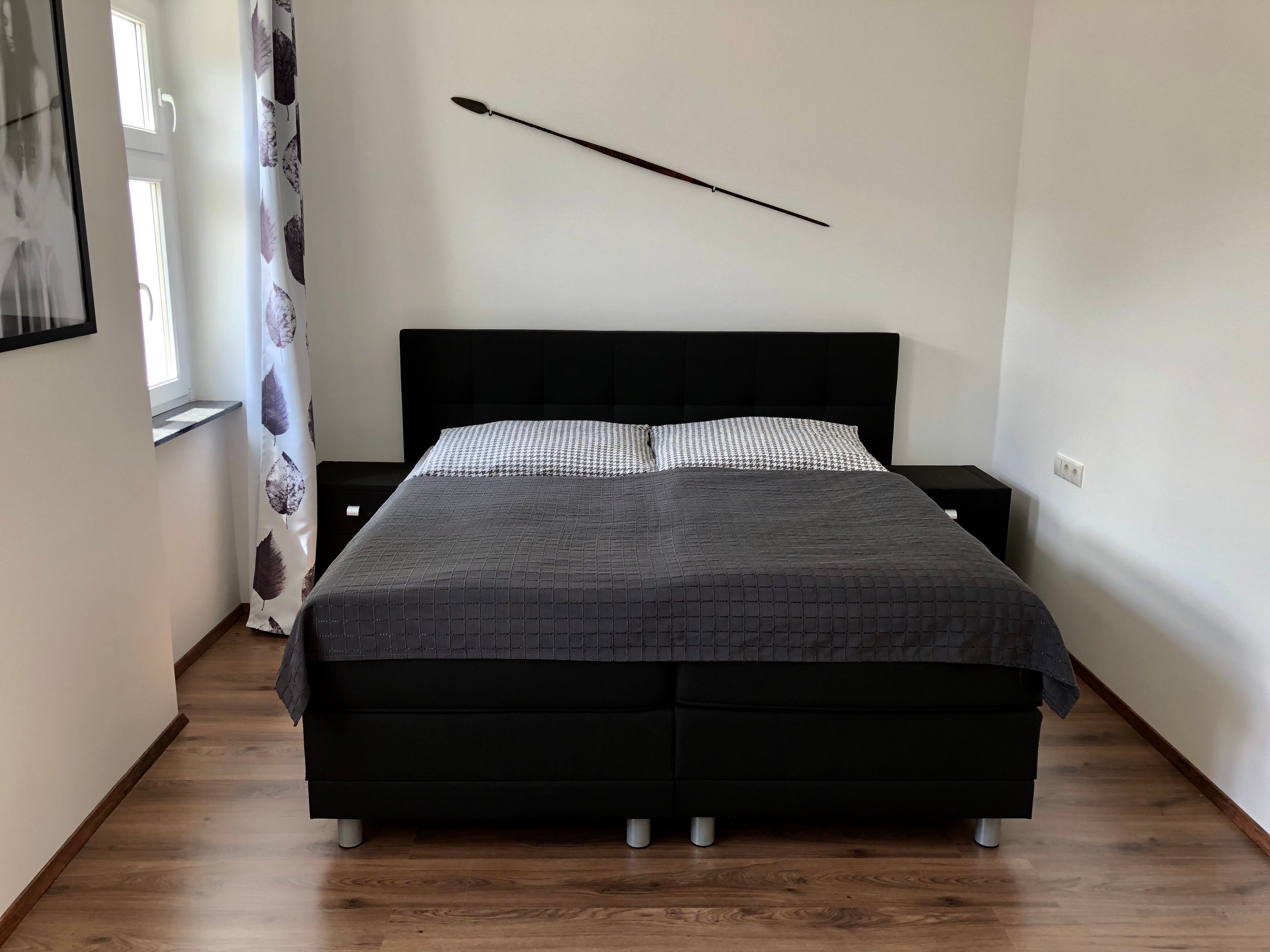 Modern bedroom with a large bed, gray comforter and a spear on the wall.