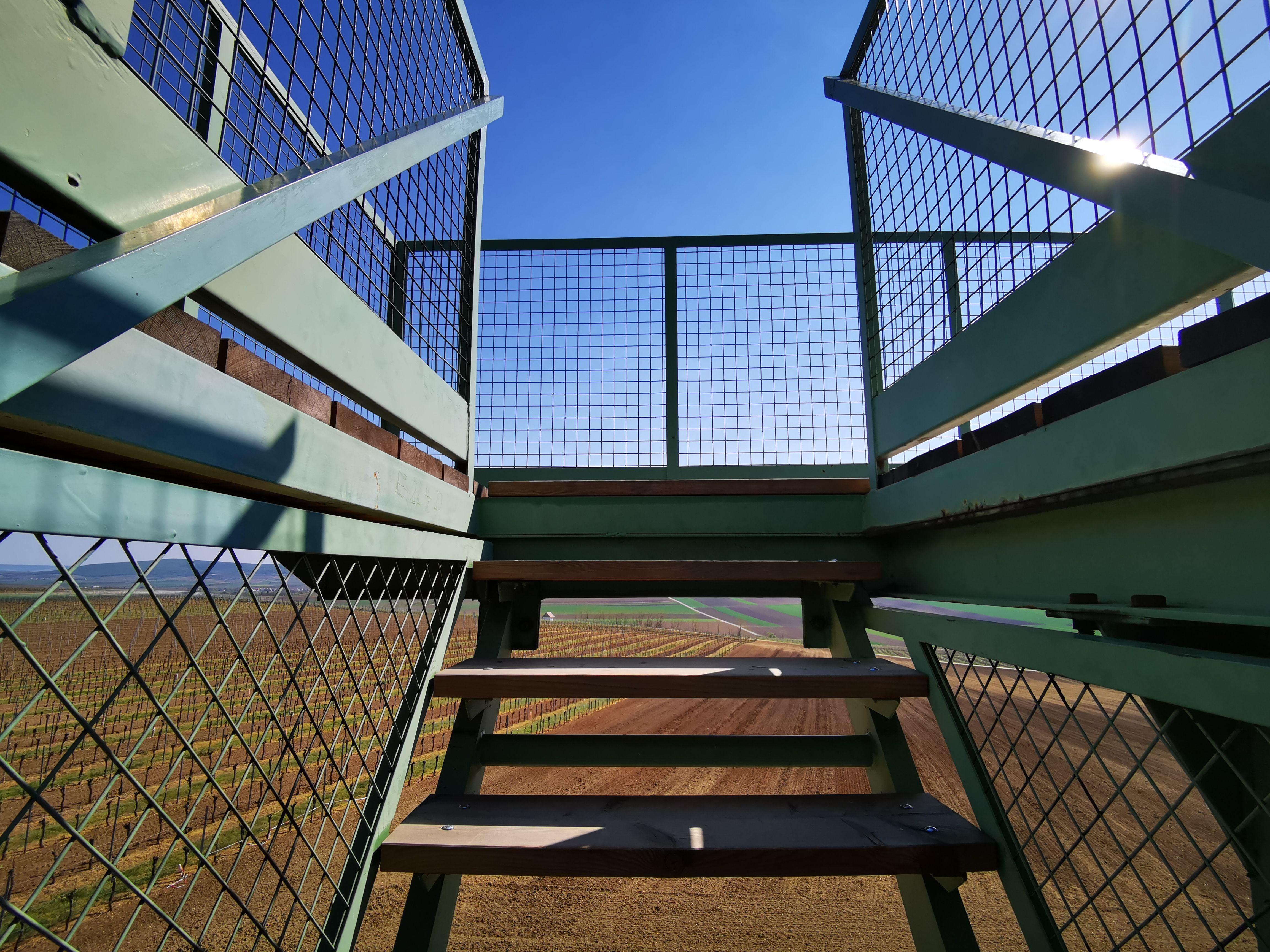 View of fields and blue sky from a staircase with metal railings.