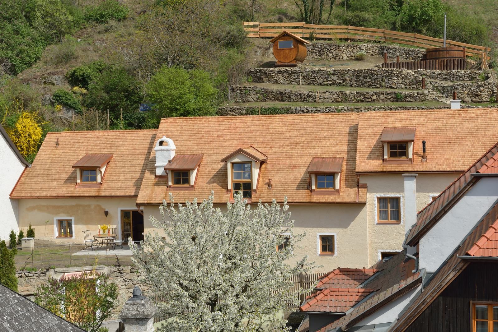 Traditional house with blossoming tree in the foreground, surrounded by green hills.