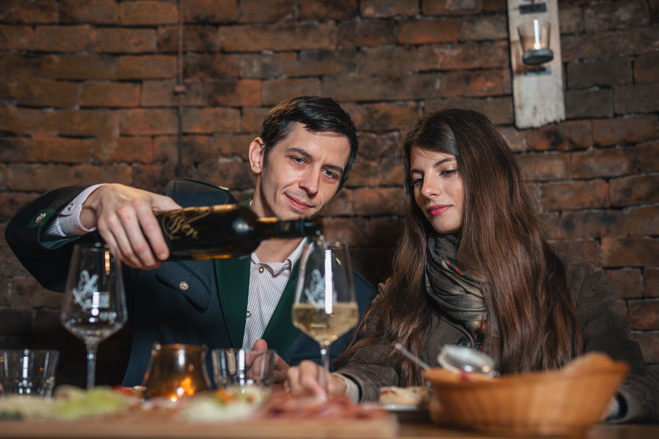 A man pours wine for a woman in a rustic room.