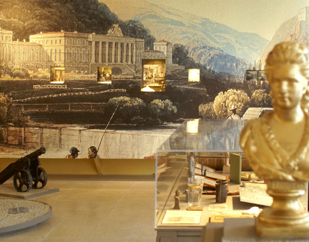 Interior view of a museum with bust, cannon and mural.