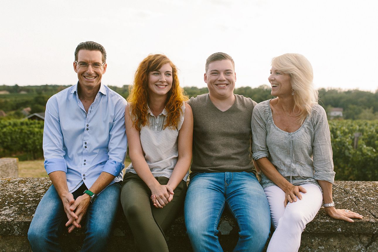Four people sit smiling on a wall outside.