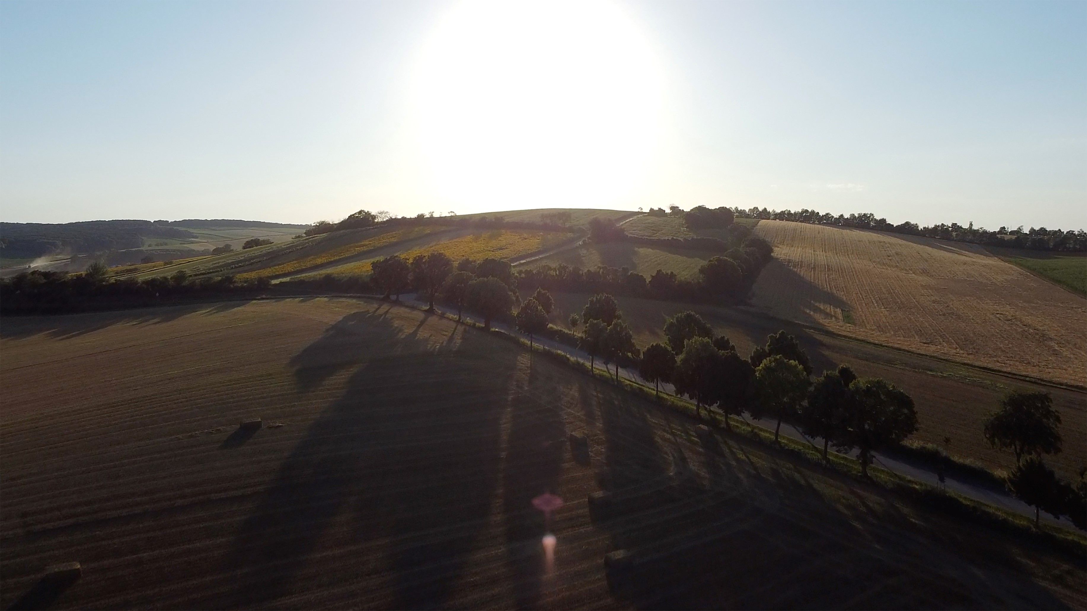 Sunset over a hilly landscape with fields and trees.