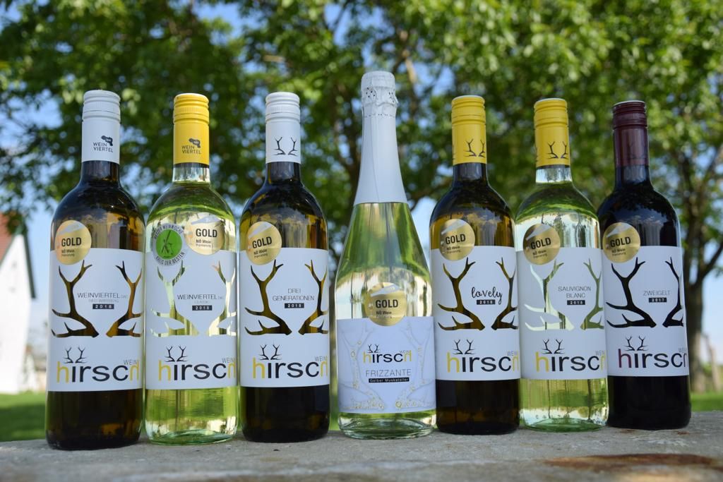 Six Hirsch brand wine bottles on an outdoor table.