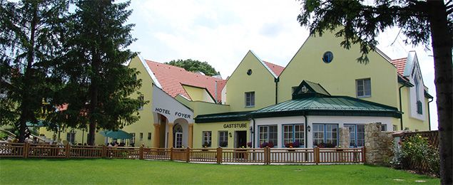 Yellow building with hotel and restaurant, surrounded by trees and lawn.