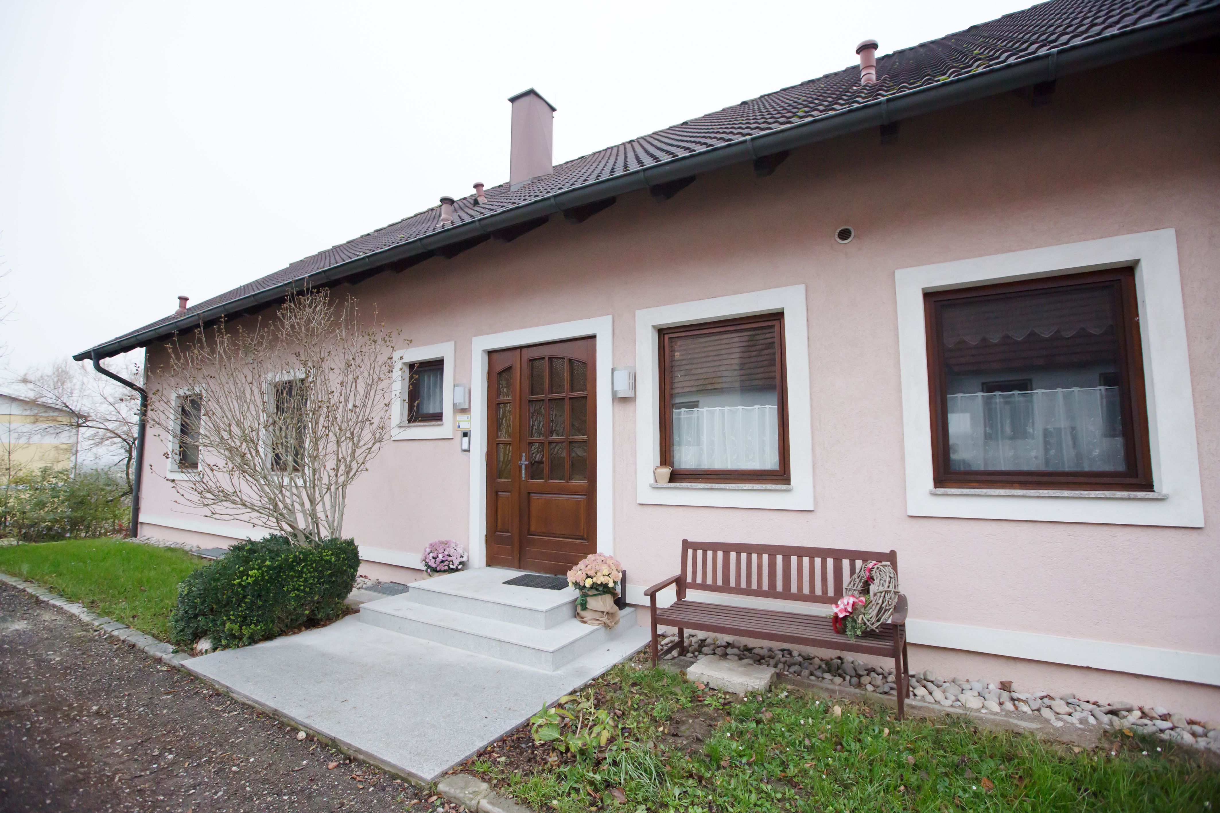 Entrance to a pink-painted vacation apartment with a wooden door, two windows and a wooden bench next to it.