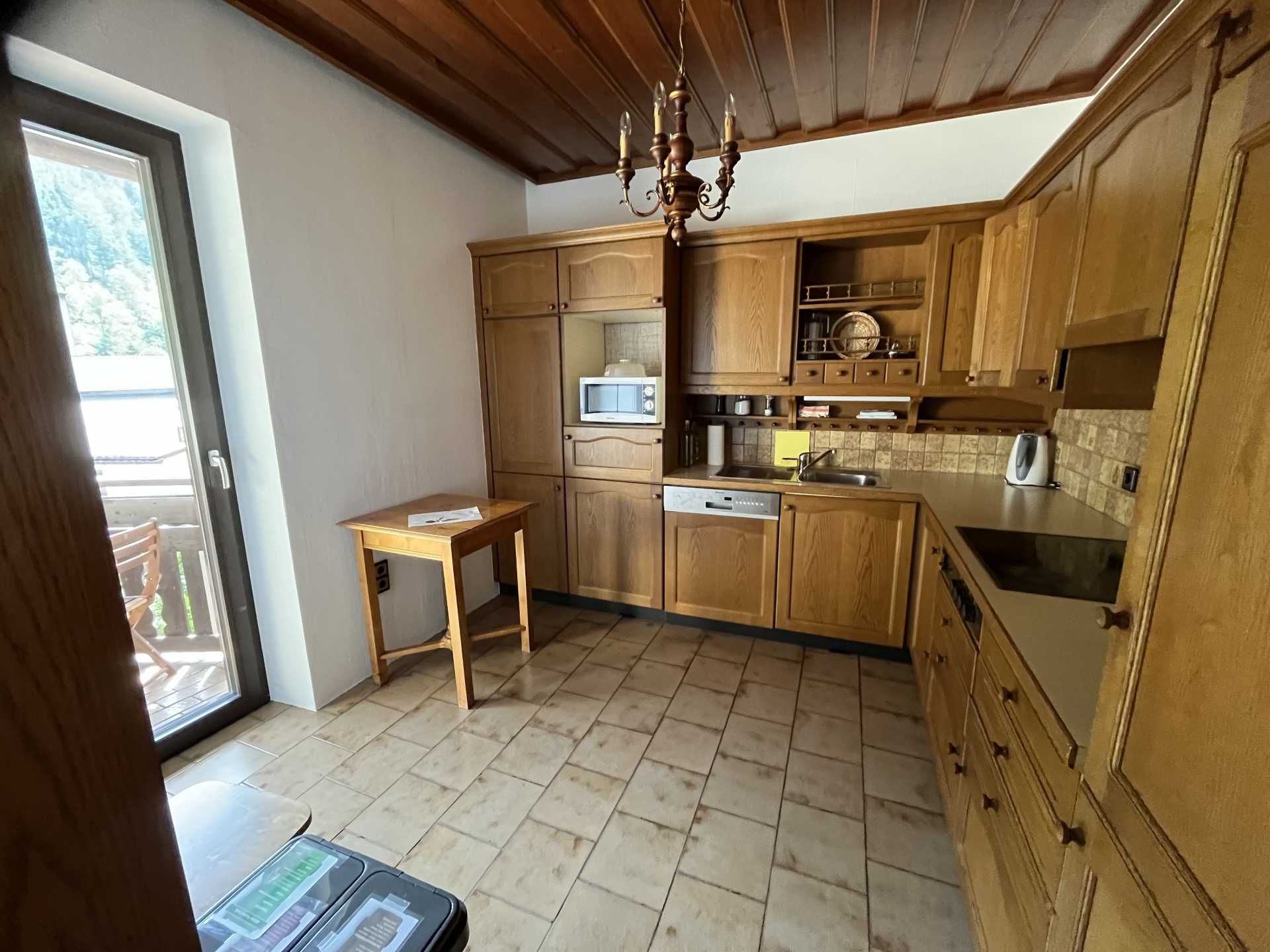 Kitchen with wooden furniture and tiled floor, view of balcony with chairs.