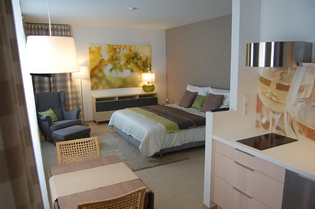 Modern apartment with bed, armchair, table and kitchenette.